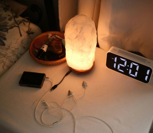 슬립테크로 재정비되는 우리의 밤, 수면 건강 관리 트렌드 뜬다 Nightstand with a lamp, clock, and chargers.