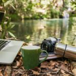 디지털 디톡스, 스트레스를 줄이고 삶의 질을 높이는 첫걸음 Laptop, camera, and mug by a forest stream