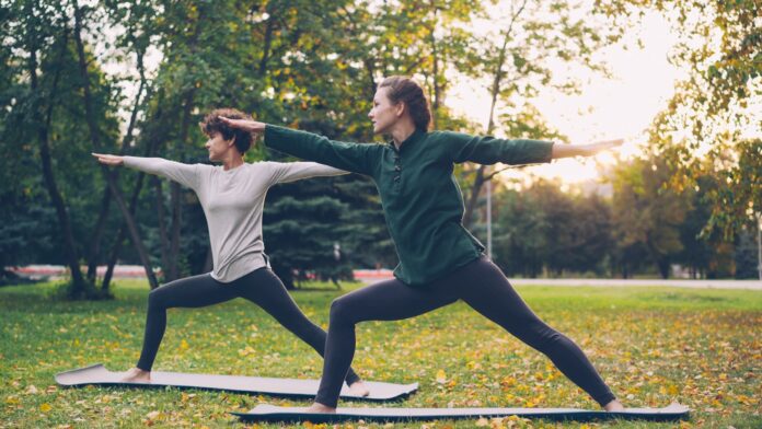 Two women practicing yoga warrior pose outdoors.